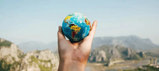 A person's hand holding small globe in front of mountains